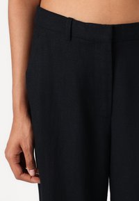 Donkerblauwe linnen broeken met een rechte snit. Voorzien van een platte voorkant, riemlussen en een zichtbare zijnaad. De textuur lijkt glad te zijn.