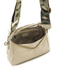 Bolso de cuero crema con un acabado texturizado, cierre con cremallera y un interior de tela a rayas. Cuenta con una correa ajustable con un patrón y herrajes metálicos.