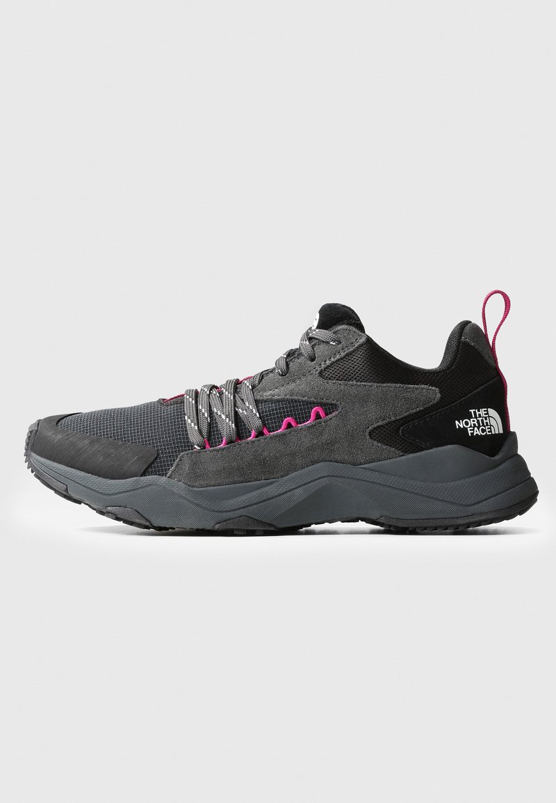 Scarpa sportiva con tomaia in tessuto grigio e dettagli in suede nero, lacci rosa e suola in gomma nera robusta. Logo del noto marchio sulla parte posteriore.