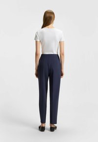 White short-sleeve top paired with navy high-waisted trousers, featuring pleats and a smooth texture, complemented by flat black shoes.
