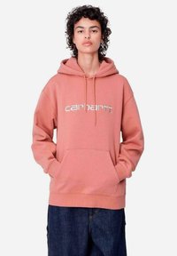 Sudadera de forro polar rosa con un gran bolsillo frontal, capucha con cordón y logo plateado de "Carhartt". Presenta puños y dobladillo acanalados.