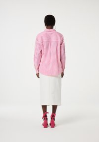 Striped pink and white oversized shirt with long sleeves, paired with a white knee-length skirt and pink heeled shoes with bows.