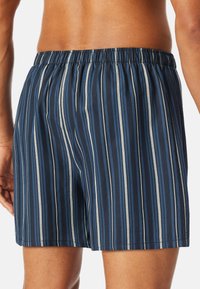 Blauwe gestreepte zwembroek met een elastische tailleband, voorzien van verticale strepen in marineblauw en lichtblauw, ontworpen voor comfort en beweeglijkheid.