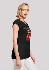 Zwarte katoen t-shirt met een logo van rode lippen, voorzien van witte accenten en gouden tekst erboven. Korte mouwen en een relaxte pasvorm.