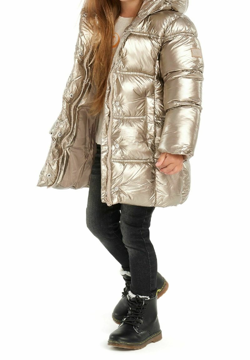 Kurtka puchowa w metalicznej złotej barwie z kapturem, zamkiem z przodu i zatrzaskami. Połączona z czarnymi obcisłymi dżinsami i czarnymi lace-up butami z futrzanym wykończeniem.