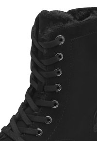 Gros plan sur une botte d'hiver noire avec des lacets épais, des œillets en métal et une doublure intérieure douce et moelleuse visible sur le bord supérieur.