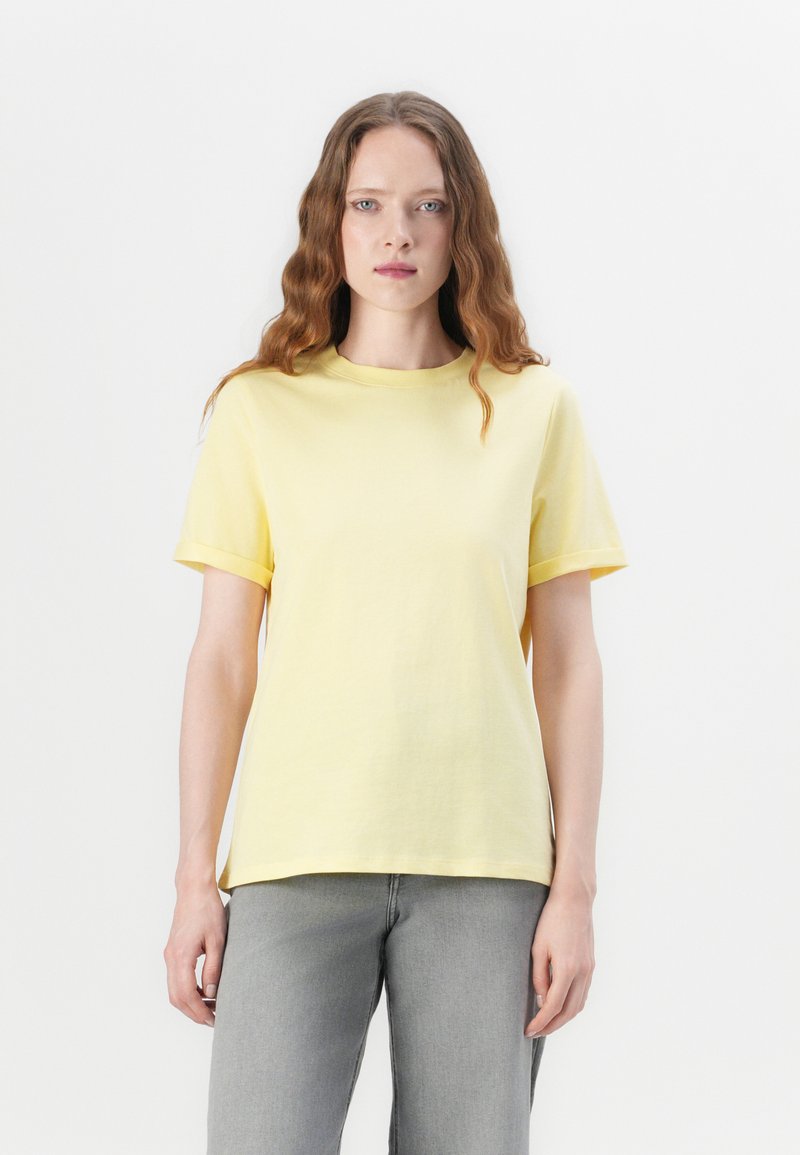 T-shirt en coton jaune avec un col rond et des manches courtes. Présente une coupe décontractée et une texture lisse. Associé à un jean en denim gris.