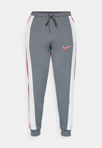 Pantalones deportivos grises con rayas laterales en blanco y rojo, cintura elástica con cordón y pequeño logo rojo de Nike en el muslo derecho.