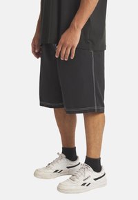 Mustat shortsit valkoisilla ompeleet, joissa on rento istuvuus ja sivutaskut. Yhdistetty valkoisiin urheilujalkineisiin ja mustiin nilkkasukkia.