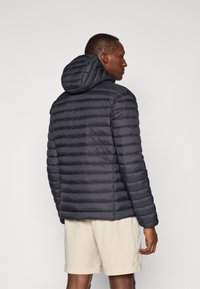 Dark padded jacket with a hood, featuring horizontal quilted design and a smooth texture. Worn over light-colored shorts.