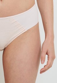 Brief bikini rosa chiaro con tessuto liscio e pannello testurizzato sul lato. Design semplice con materiali e cuciture a contrasto.