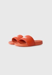 Pair of orange slide sandals with white crocodile logo on straps, textured footbed, and "Lacoste" branding on side.