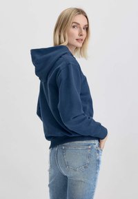 Felpa di un blu navy con un ampio cappuccio e polsini a coste, abbinata a jeans in denim azzurro chiaro. La felpa ha una vestibilità rilassata e una trama liscia.