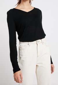 Svart v-ringad långärmad tröja i mjukt tyg, kombinerad med högmidjade ljusa jeans med knapp- och dragkedjestängning.