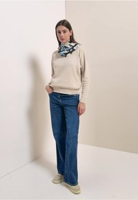 Beige sweater, mørkeblå vidde jeans, limegrønne sneakers og et mønstret sort tørklæde med blå accenter. Simpelt, afslappet outfit på en model.