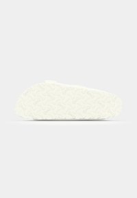 White slip-on shoe with a textured rubber sole displaying a wavy pattern, smooth upper surface, and minimalistic design.