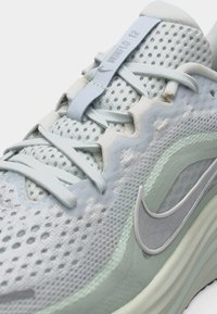 Κοντινό πλάνο ενός ανοιχτόγαλανου παπουτσιού τρεξίματος Nike Winflo 12 με επάνω μέρος από δίχτυ, κλείσιμο με κορδόνια και αντανακλαστικό λογότυπο swoosh στο πλάι.