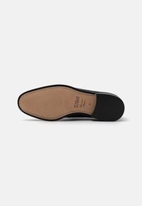Black leather shoe sole with a smooth black edge, beige middle featuring textured lines, and stitching detail along the perimeter.