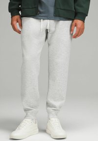 Grijze katoenen sweatpants met een elastische tailleband en witte trekkoordjes, gecombineerd met witte sneakers, tegen een neutrale achtergrond.