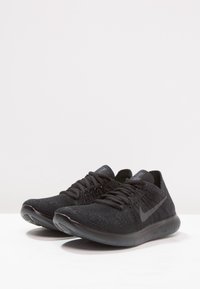 Chaussures de sport noires avec une tige en maille texturée, dotées de lacets noirs et d'un logo Swoosh bien visible. La semelle est élégante et arrondie.