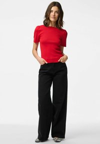 Top rosso aderente con maniche a sbuffo, texture a costine, abbinato a pantaloni neri a vita alta e larghi e scarpe a righe bianche e nere.