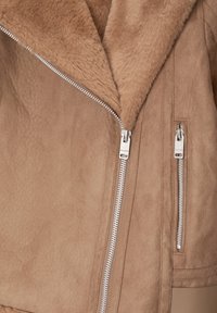 Tan faux suede jacket with a plush, fur-lined collar, featuring two silver zippers and a smooth texture.