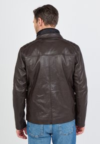 Bruine leren jack met een gladde textuur, hoge kraag en gewatteerde schouderdetails. Heeft een klassieke snit en gestikte naden.