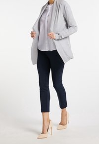 Light gray cardigan with ribbed detailing, worn over a white blouse and navy slim-fit pants. Beige high-heeled shoes complete the outfit.