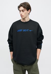 Μαύρο φαρδύ φούτερ από μαλακό ύφασμα, με μπλε κεντημένο λογότυπο "JUST DO IT." και σήμα Nike. Μανσέτες και τελείωμα με ριμπ ύφασμα.