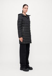Melna pūkaina jaka ar rāvējslēdzi priekšā, kapuci un sānu kabatām. Ar horizontālām šuvēm un zeltainiem aksesuāriem. Elegants un izolēts dizains.