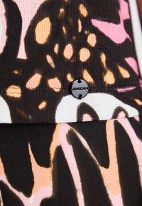 Abstrakt mønstrede stoffer med nuancer af sort, pink og orange. En sort metallisk knap med "Marc Cain" logo fremhæver designet.