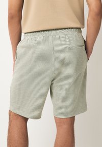 Pantalones cortos a rayas verdes y blancas, tela ligera, cintura elástica, bolsillos laterales y un único bolsillo trasero. Corte entallado con borde dobladillado.