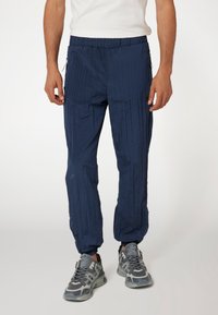 Jūrų laivyno spalvos, lengvi kelnių su tekstūruotu paviršiumi, elastiniu juosmeniu, šoninėmis užtrauktukais ir siaurėjančiais rankogaliais, skirti komfortui ir judrumui.