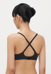 Zwarte beha met gekruiste bandjes op de rug. Gemaakt van een soepele stof, voorzien van een haaksluiting en verstelbare bandjes voor een comfortabele pasvorm.