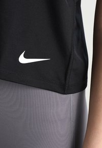 Sort atletisk skjorte med korte ærmer, med et hvidt Nike-logo på venstre side, kombineret med grå, teksturerede leggings.