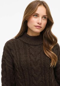 Ciemnobrązowy sweter o splocie warkoczowym z wysokim kołnierzem i fakturowanym wzorem, prezentujący miękką, grubą konstrukcję dzianiny.