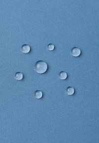 Droaturi clare de apă de dimensiuni variate se află pe un material texturat de culoare albastră, evidențiindu-și formele rotunde și suprafețele reflective.