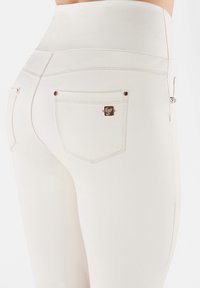 Valkoiset korkea vyötäröiset farkut, joissa on sileä pinta, kaksi takataskua ja ruusukultaiset yksityiskohdat taskujen reunassa.