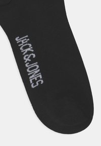 Calzino di cotone nero con una texture liscia. Presenta il logo bianco "JACK & JONES" lavorato sul lato, punta arrotondata e senza motivi visibili.