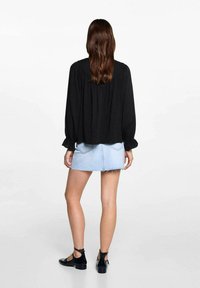 Blusa nera a maniche lunghe con dettaglio arricciato sul retro, abbinata a una mini gonna in denim azzurro. Le scarpe nere con cinturino alla caviglia completano l'outfit.