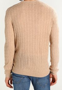 Beige kabelstickad tröja med långa ärmar, rund halsringning och ribbade muddar. Mjuk textur och figurnära design. Bilden visar baksidan.