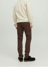Giacca di denim beige con dettagli a bottoni, abbinata a pantaloni marroni scuri. Scarpe in camoscio nero con suola in gomma. Design semplice e contemporaneo.