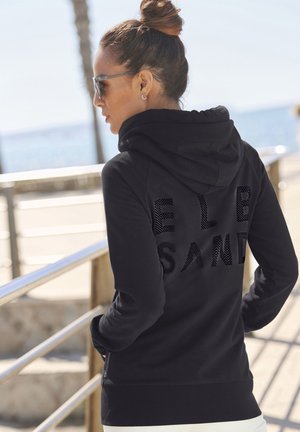 Schwarzer Hoodie mit strukturiertem Muster und dem Schriftzug "EL SAND" auf dem Rücken. Er besteht aus einem weichen Material, hat lange Ärmel und einen lässigen Schnitt.