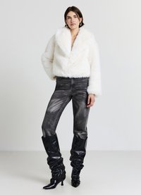 Weiße, kurz geschnittene Jacke aus Kunstpelz mit breiten Revers, kombiniert mit hoch taillierten, dunkelgrauen Jeans und schwarzen, lässigen kniehohen Stiefeln.