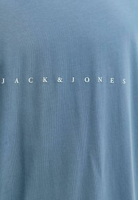 Hele sinine puuvillane t-särk, mille rinnal on valge tekst "JACK & JONES". Pehme tekstuur ja lõdvestunud lõige ümara kaelusega.