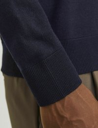 Marine gebreide trui met geribde manchetten, close-up dat de textuur toont. De manchette heeft een strakke patronen; de mouwstof lijkt zacht en glad.