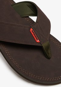 Chanclas de cuero marrón con correas de tela verde oliva, costuras reforzadas y un acento de logo rojo. Superficie lisa con una correa texturizada.
