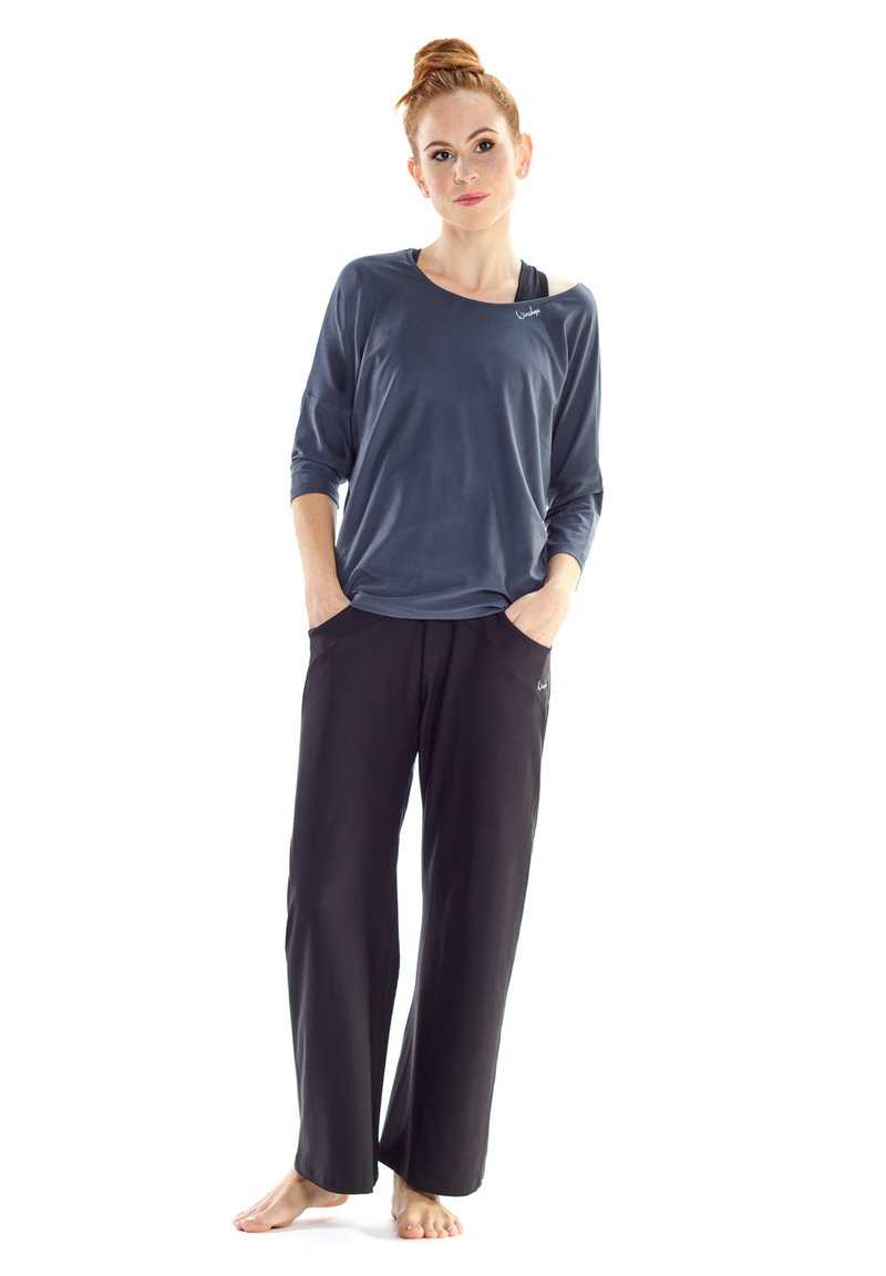 Dunkelblaues Langarmshirt mit weitem Ausschnitt, kombiniert mit lockeren schwarzen Hosen mit Seitentaschen und subtiler Markenkennzeichnung.