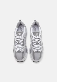 Pár šedobílých běžeckých tenisek New Balance s bílými tkaničkami, zobrazených shora na bílém pozadí.