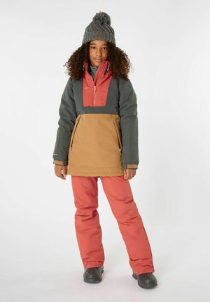 Farbige Oberbekleidung bestehend aus einer grünen und braunen Jacke mit rotem Brustpanel, kombiniert mit rosa Hosen und schwarzen wasserdichten Stiefeln.